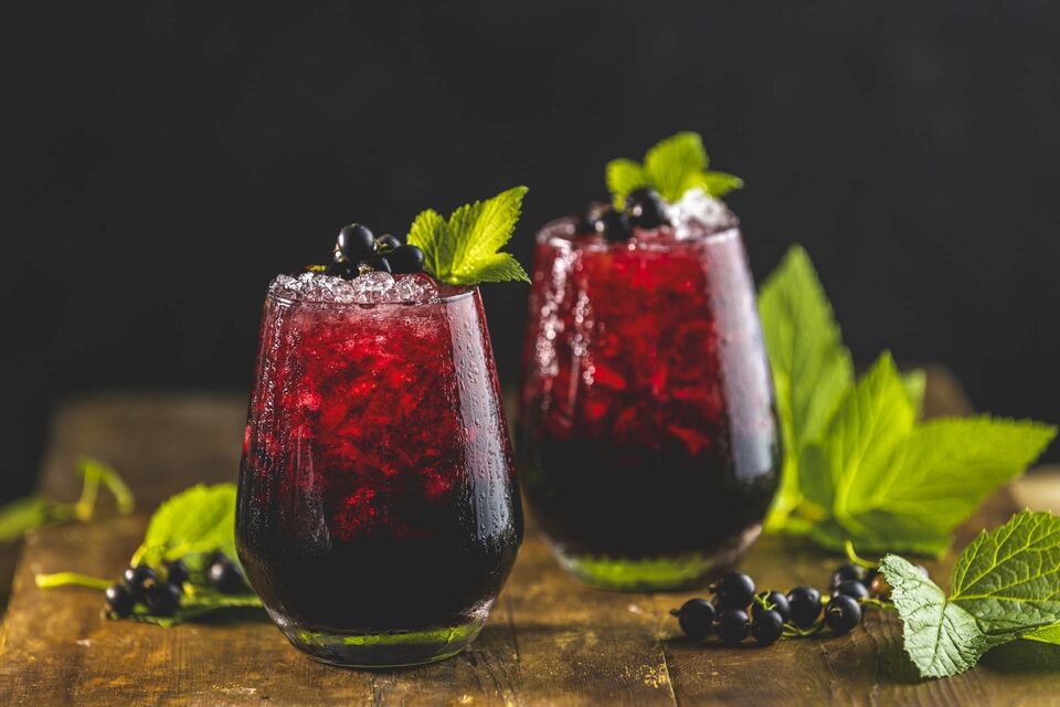 Eisgekühlte Getränke mit Cassis, Beeren und Blättern